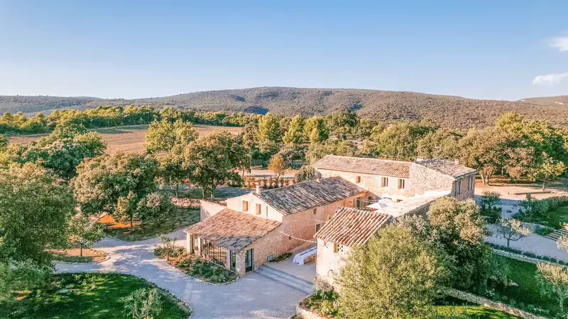 Vue aérienne des bâtiments en pierre du Mas de Florette à l’heure dorée, les collines du Luberon derrière